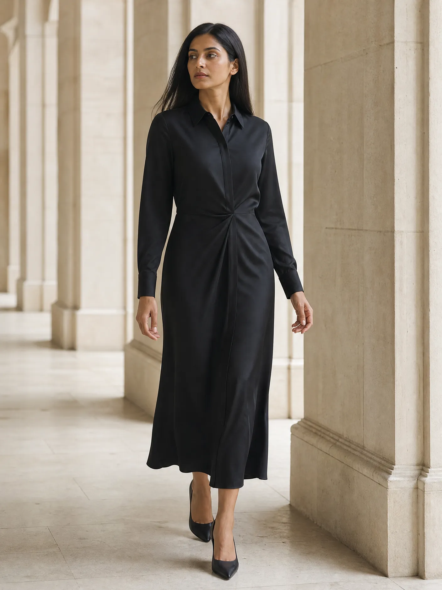 Illustration: a model in a long black shirt dress with buttoned cuffs, in a pale stone colonnade