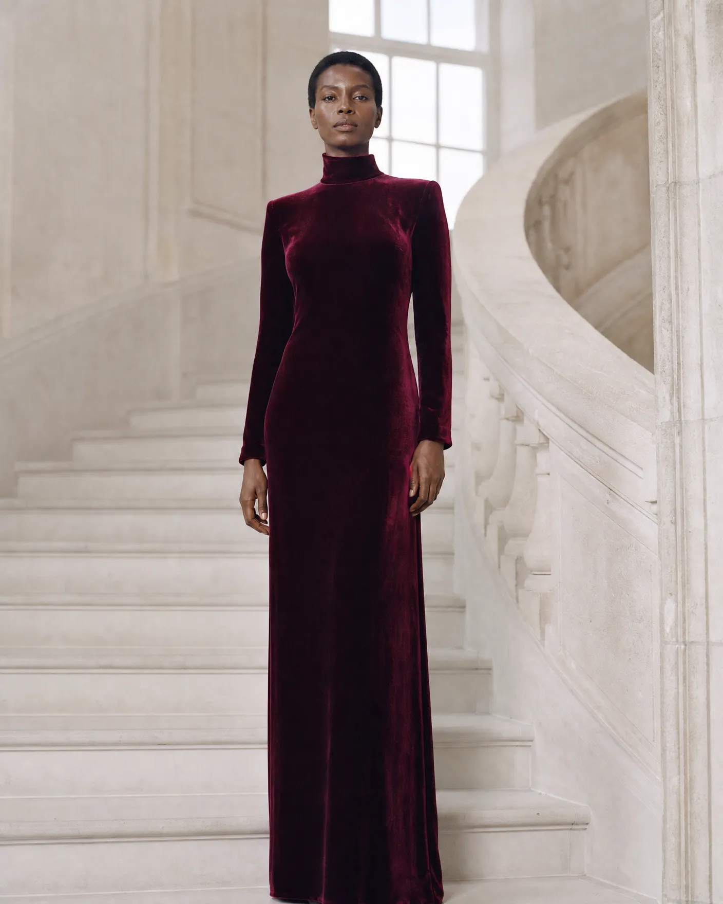 Illustration: a model in a floor-length bordeaux velvet gown on a pale stone staircase